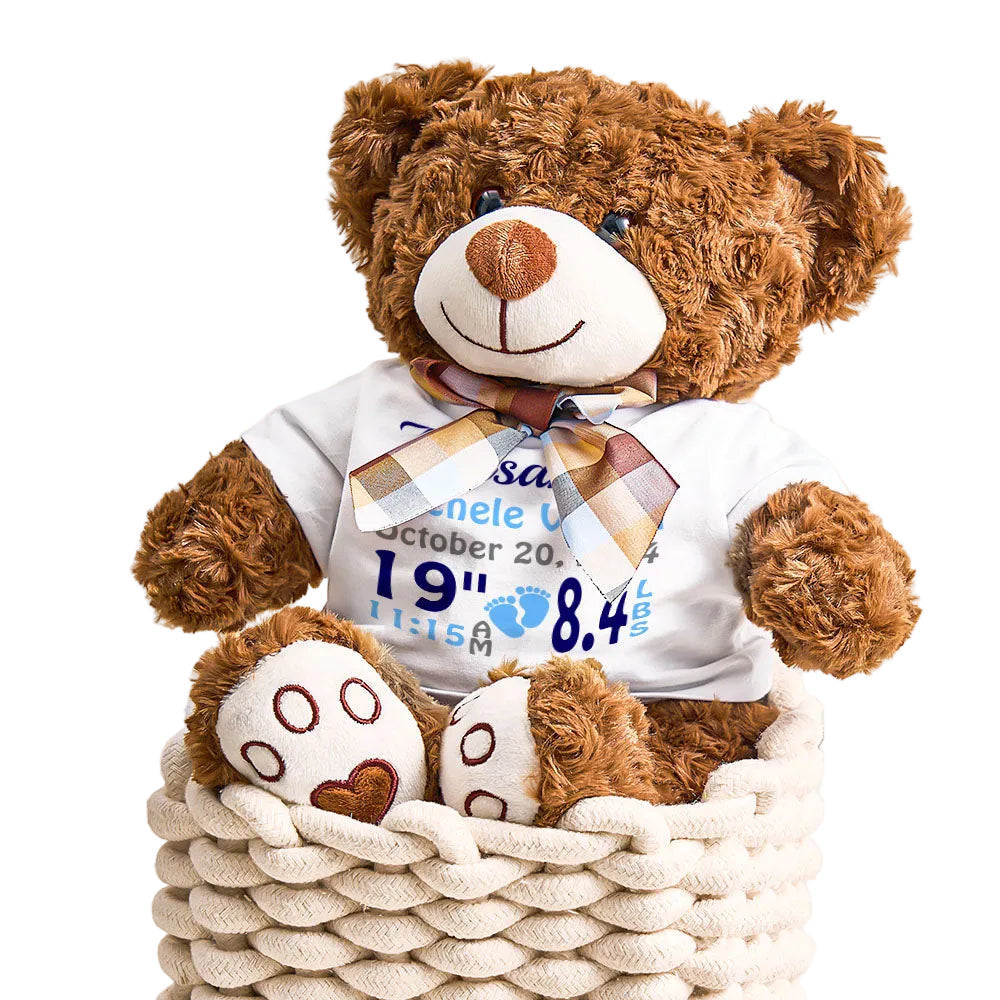 Brown teddy bear wearing a white shirt with text, sitting in a woven basket.