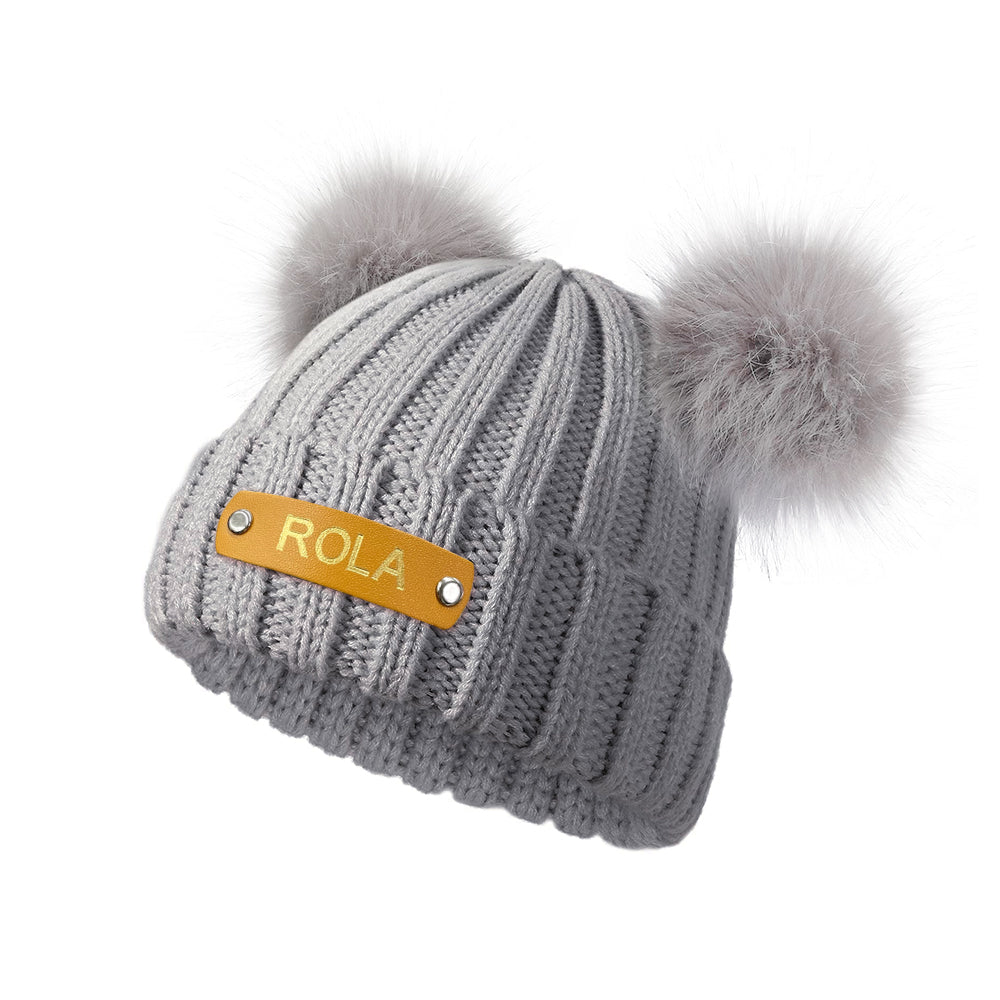 Gray knit beanie with pom-poms and a Rola label on a white background