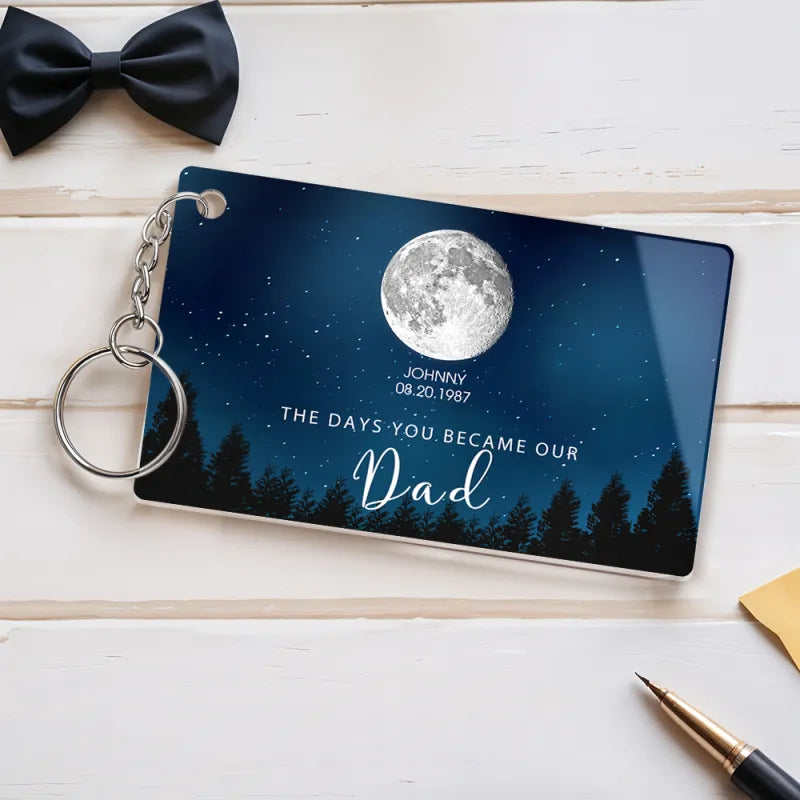 Personalized keychain with moon and tree design on a wooden surface with a bow tie and pen.