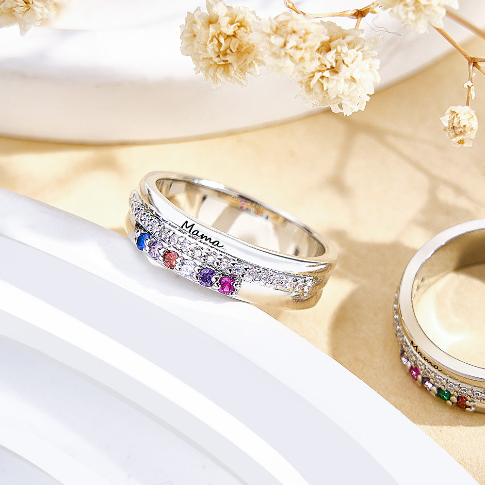 Silver ring with colorful gemstones and 'Mama' engraving on a white surface with flowers.