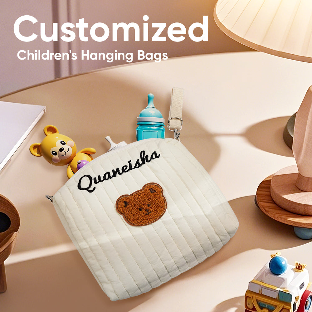 Children's hanging bag with teddy bear design and 'Quaneisha' branding on a table with toys.